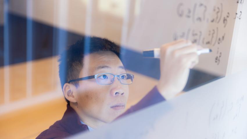 man in glasses writing on glass with an erasable marker