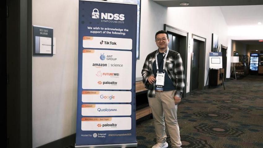 Man standing next to a roll out banner in a hallway.