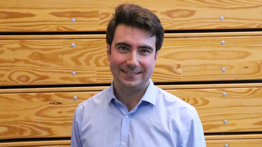 A smiling man standing in front of a wooden wall. 