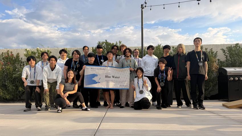 A group of people standing outside holding a banner. The banner reads "Blue Water," the team's name. 