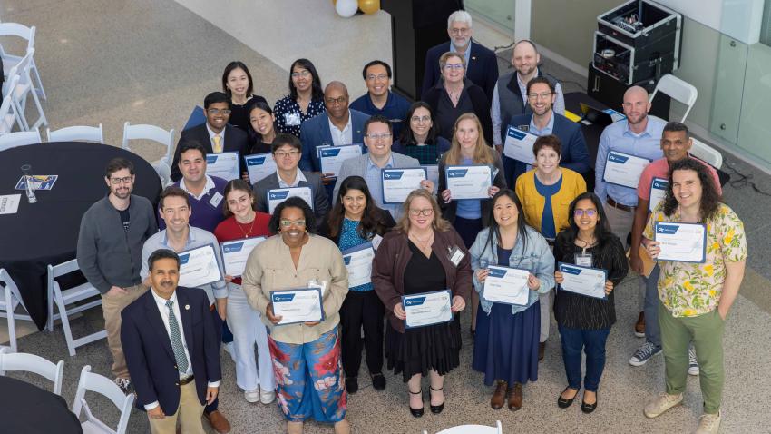 A group of smiling people looking up at the camera. They are all holding up certificates. 