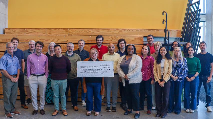 A group photo of more than a dozen people. A woman in the center is holding a large check for Klemis Kitchen, Georgia Tech's on-campus food pantry.