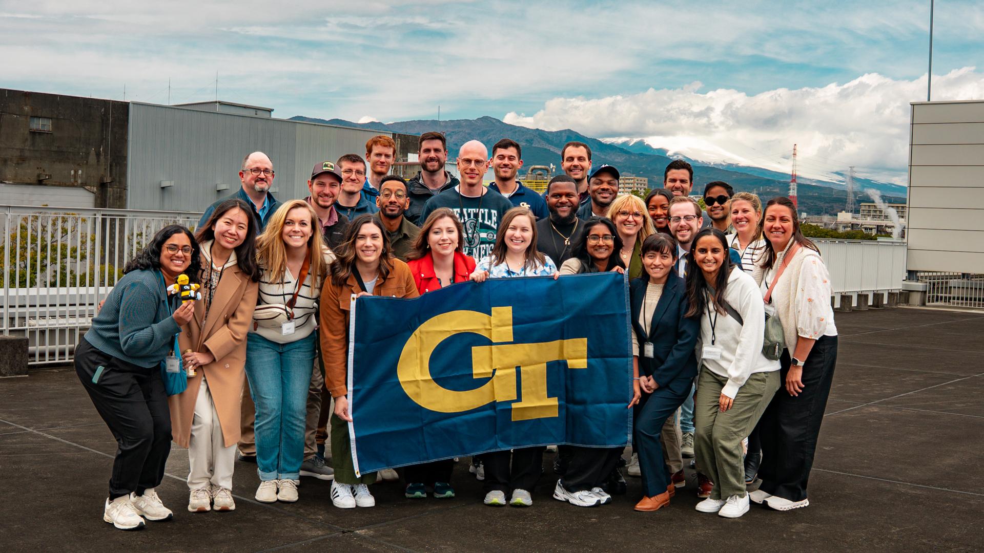 A group of people standing outside holding a Georgia Tech flag.