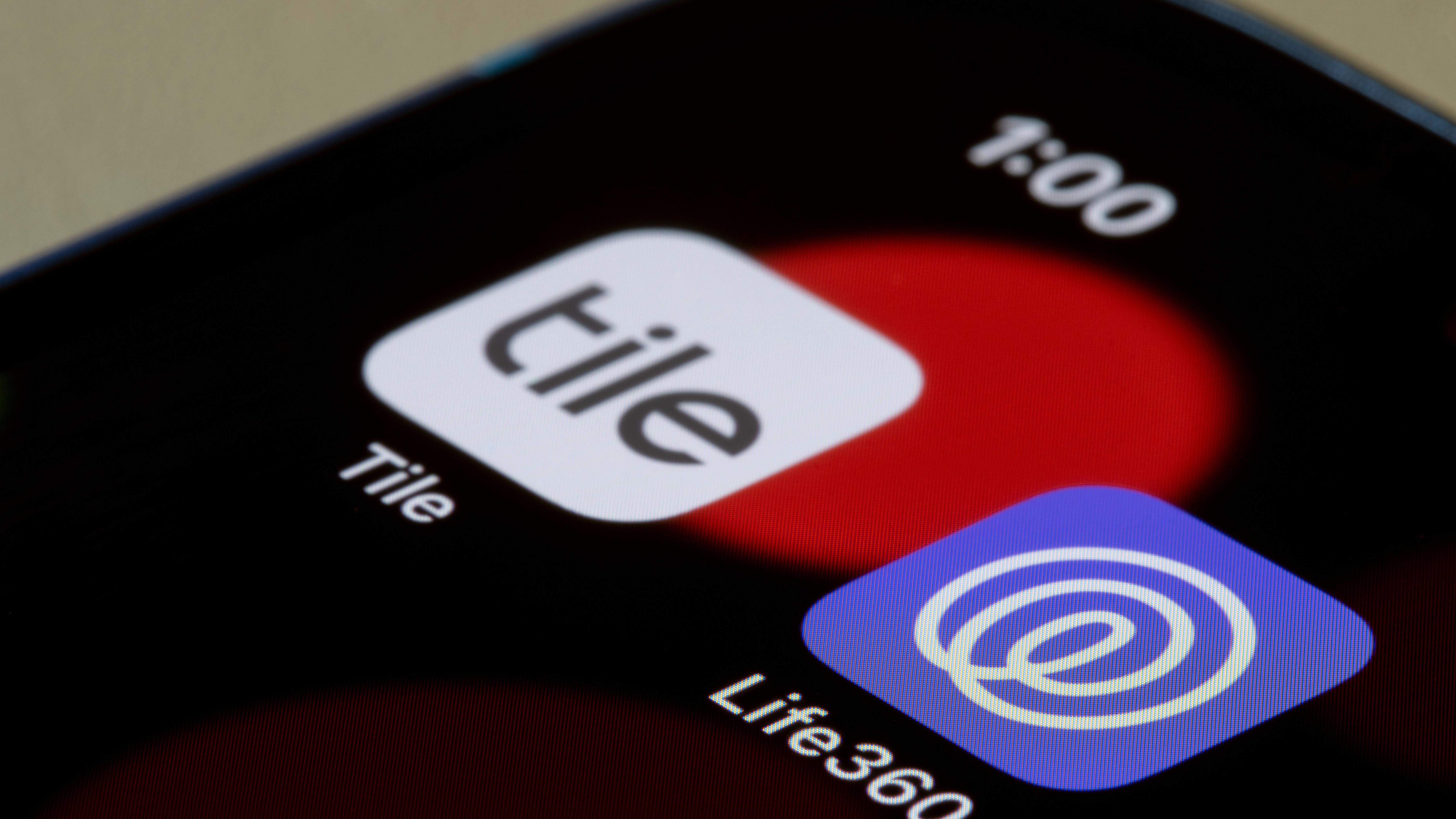 A photo of a smart phone screen showing the Tile and Life 360 apps. The time at the top of the phone says 1:00 and the phone background has a red circle.