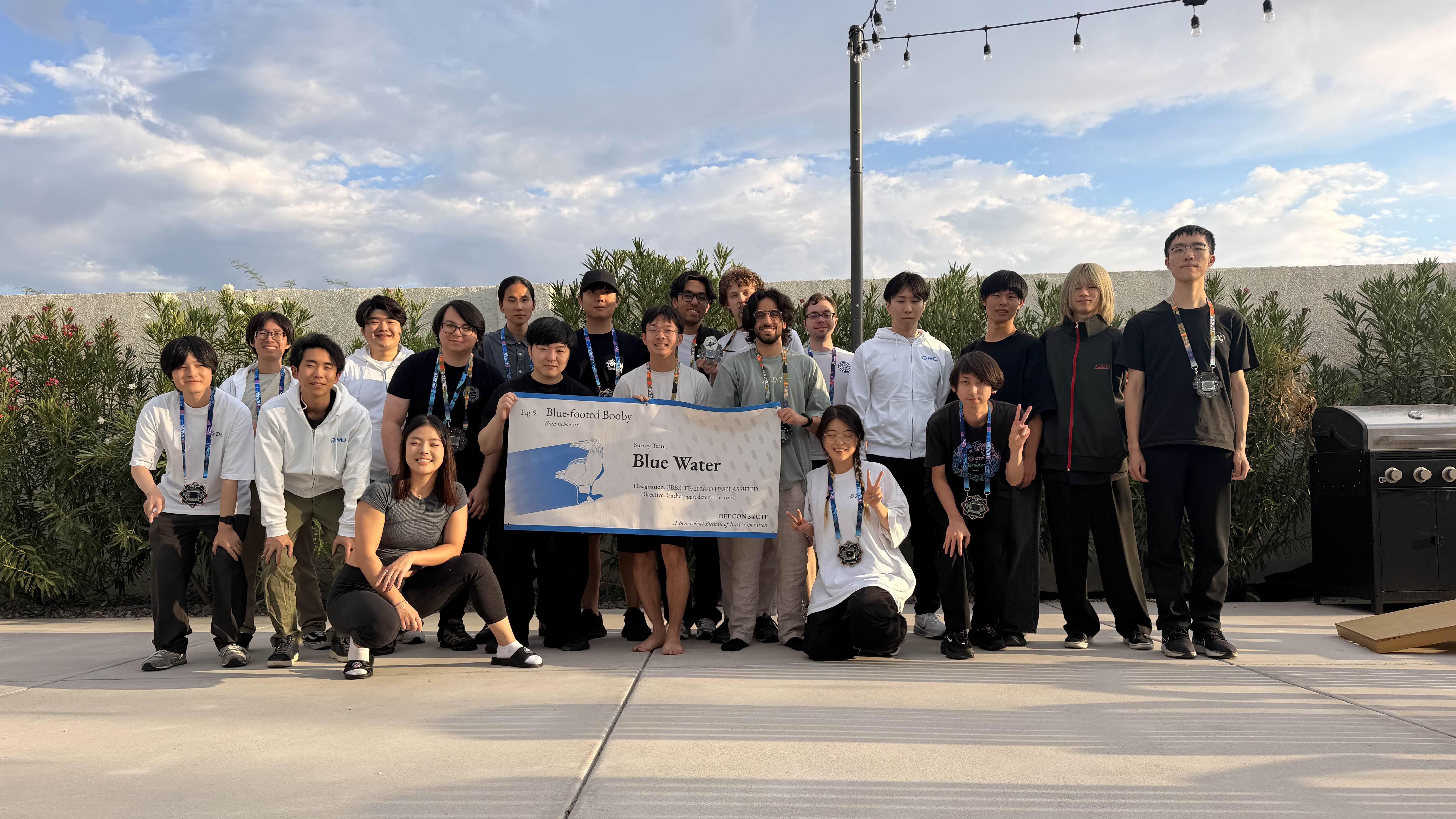 A group of people standing outside holding a banner. The banner reads "Blue Water," the team's name. 