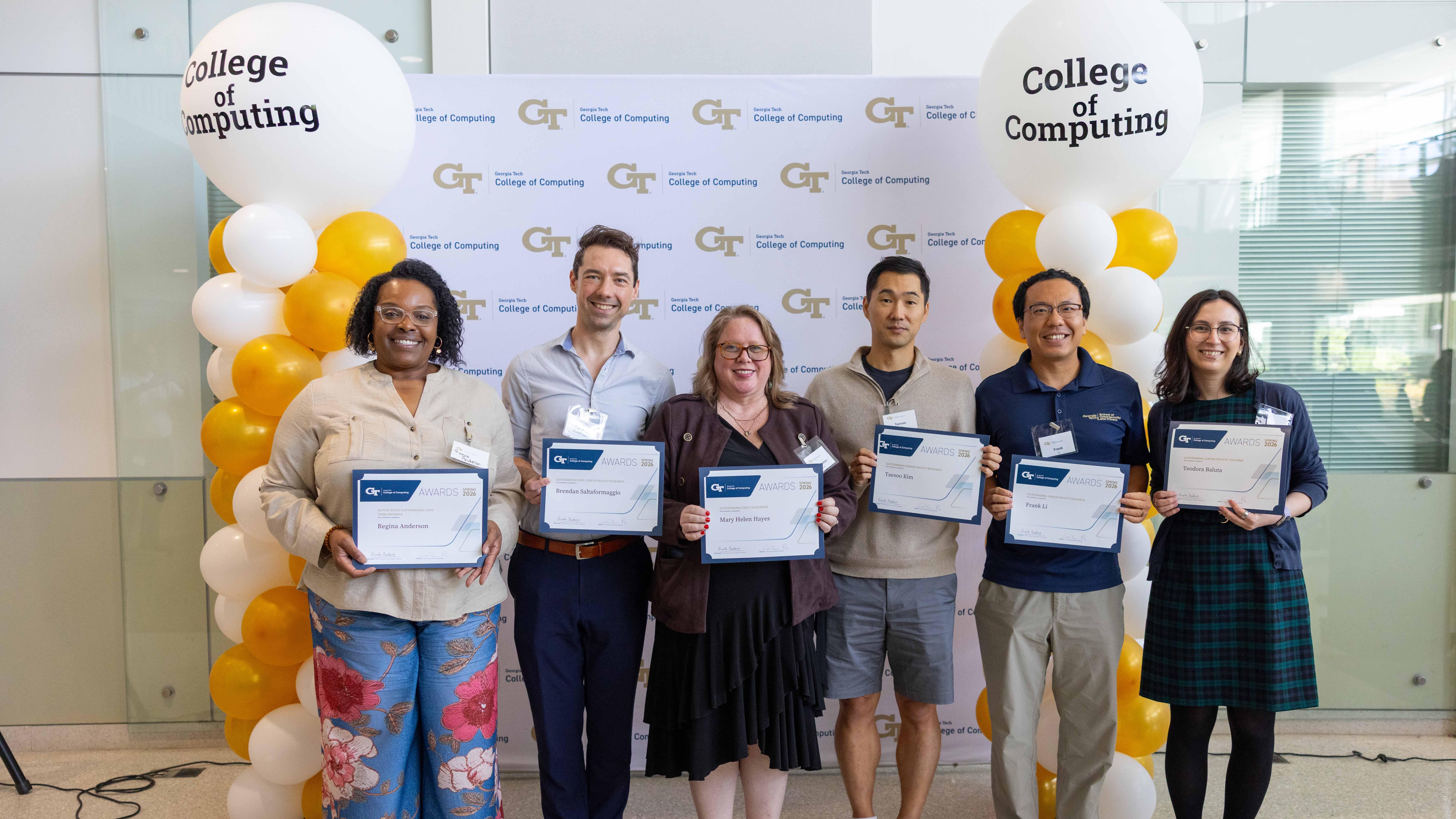 A group of people standing in front of a banner. They are all holding certificates. 